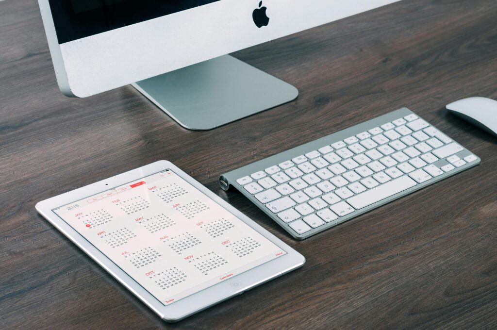 A sleek and modern office desk setup featuring an iMac, iPad with calendar, keyboard, and mouse.